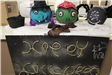 Pumpkins decorated as witch, zombie and spider. Sign reads 