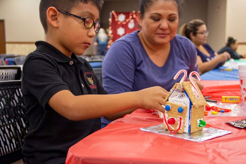 A young boy wearing glasses builds a graham cracker gingerbread house with a candy happy face