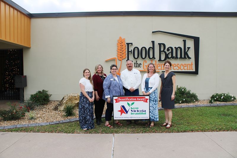Group photo in front of building with Food Bank logo and bed with flowering shrubs and boulder