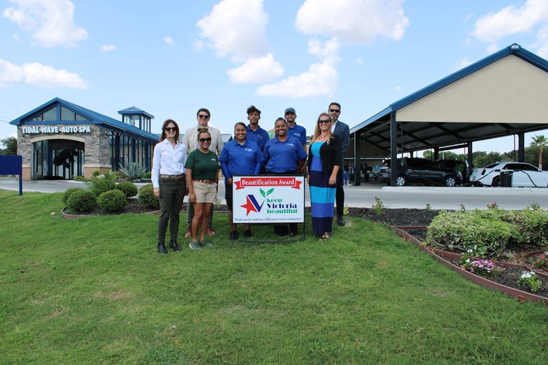 Group photo with KVB sign between flower beds with a car wash in the background