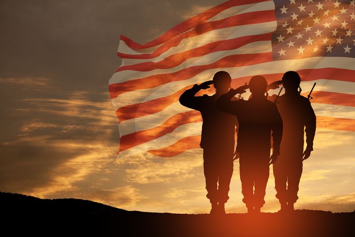 Silhouette of soldiers saluting the American flag at sunset