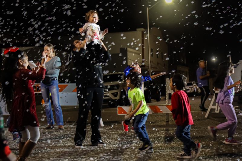 Kids run and play in foam snowflakes. A woman holds a small child up high.