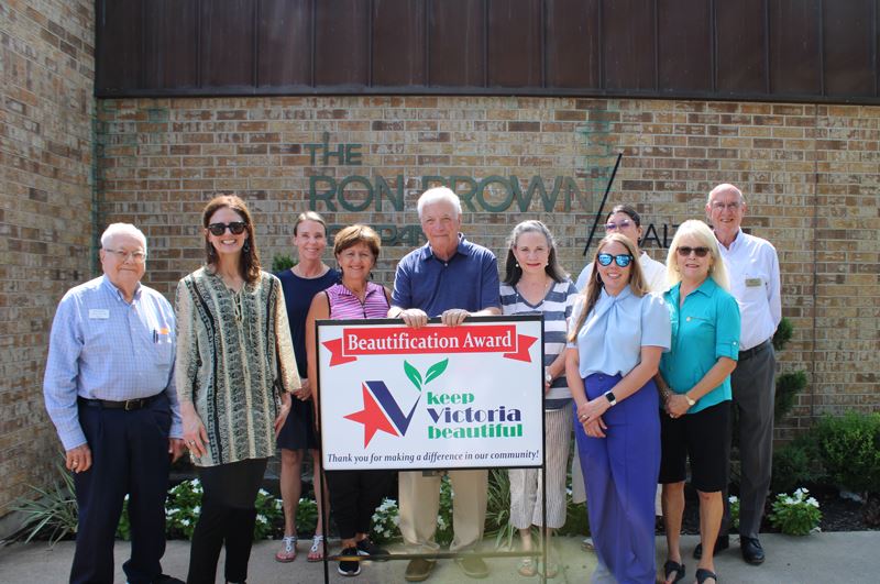 Group photo with KVB sign in front of The Ron Brown Company with flowers in background