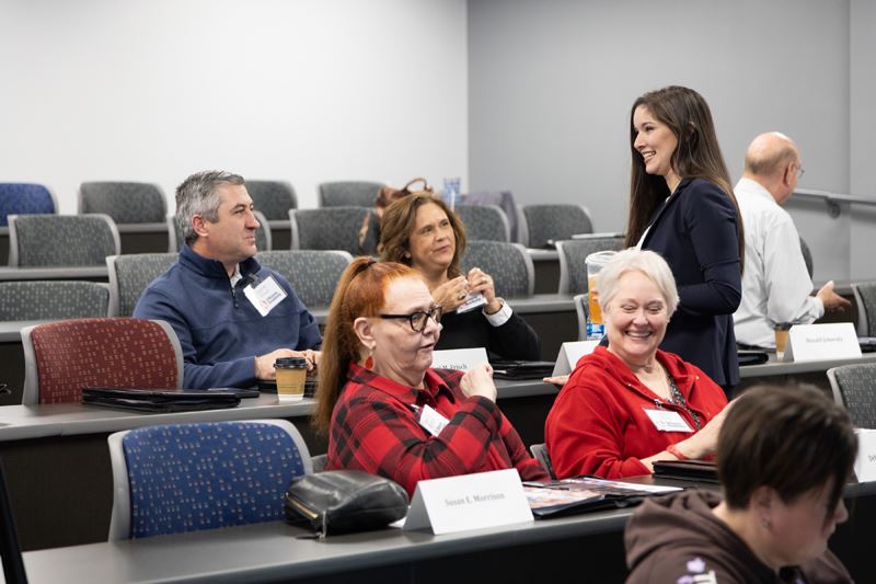 A woman visits with seated people in a small college auditorium classroom