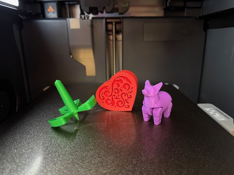 Three items created from a 3D printer including an articulated dog, a spinner, and a heart.
