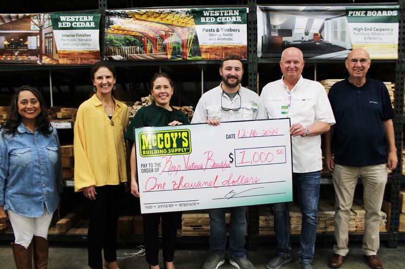 Group photo with giant check at McCoy's with lumber in the background.