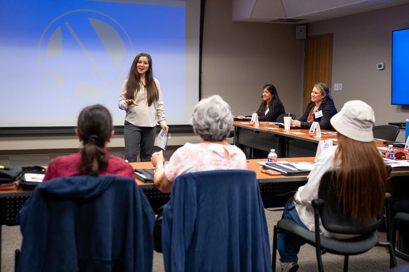 Ashley Strevel addressing seated attendees with Citizens Academy logo projected in the background