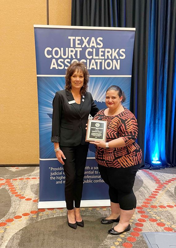 Woman holds plaque in front of TCCA backdrop. Another woman stands beside her.