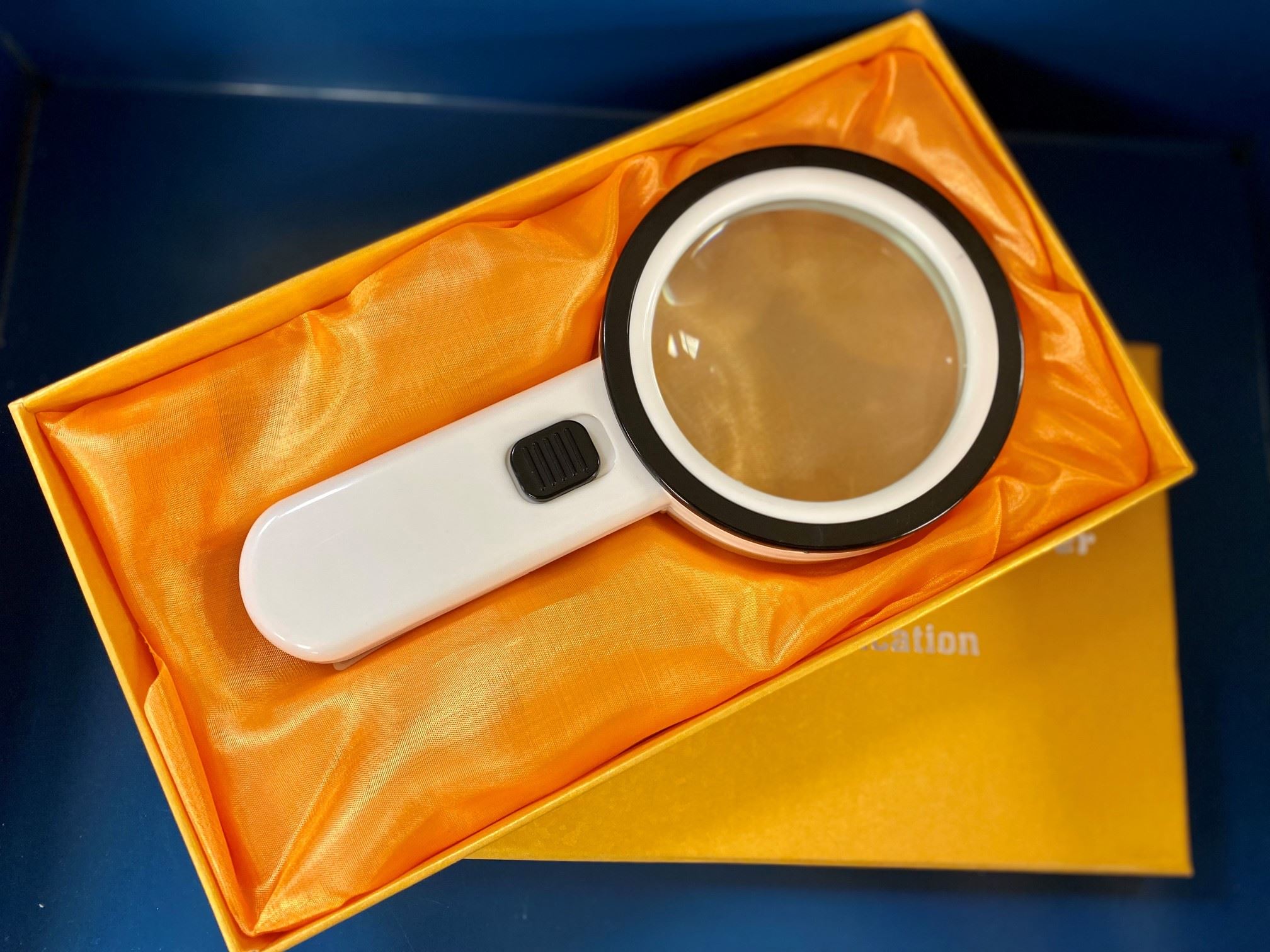 LED-backlit magnifying glass, white handle in yellow case with a blue background