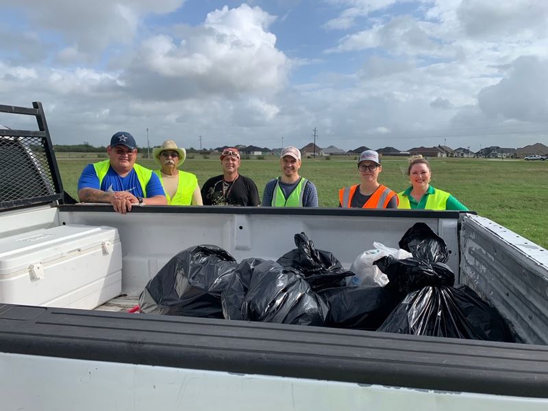 People in work vests stand near a pickup loaded with bags of trash.