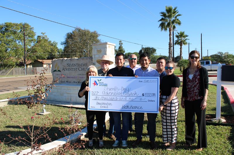 Group photo with giant check in front of stone-and-brick sign for Seventh Day Adventist Church