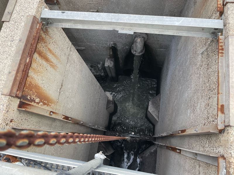 A rusty chain extends deep into a concrete pit with water flowing into it