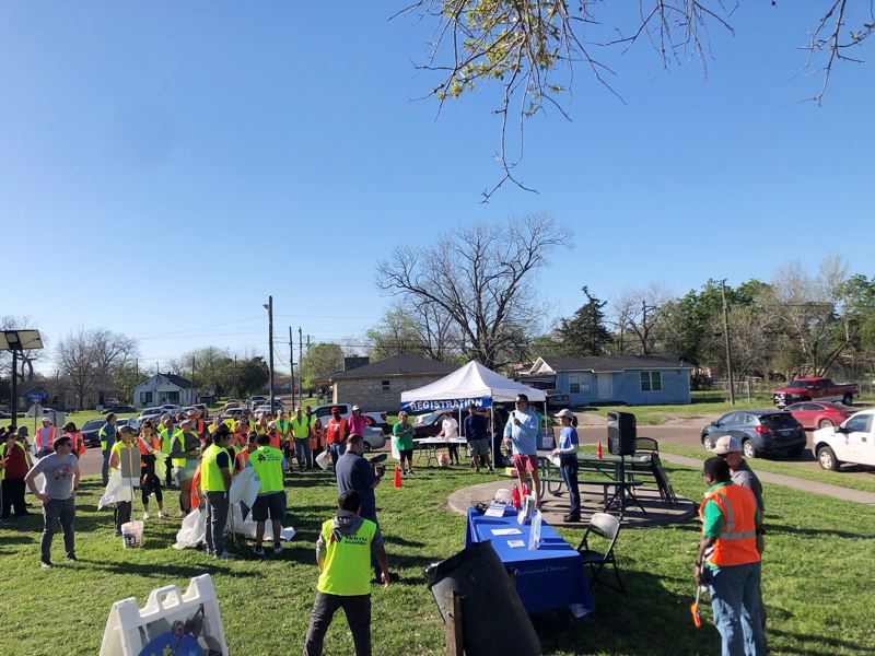 A man holding a microphone addresses a crowd in a park.