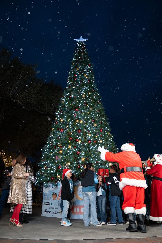 People cheering around the lighted Christmas tree downtown, including Santa and Mrs. Claus